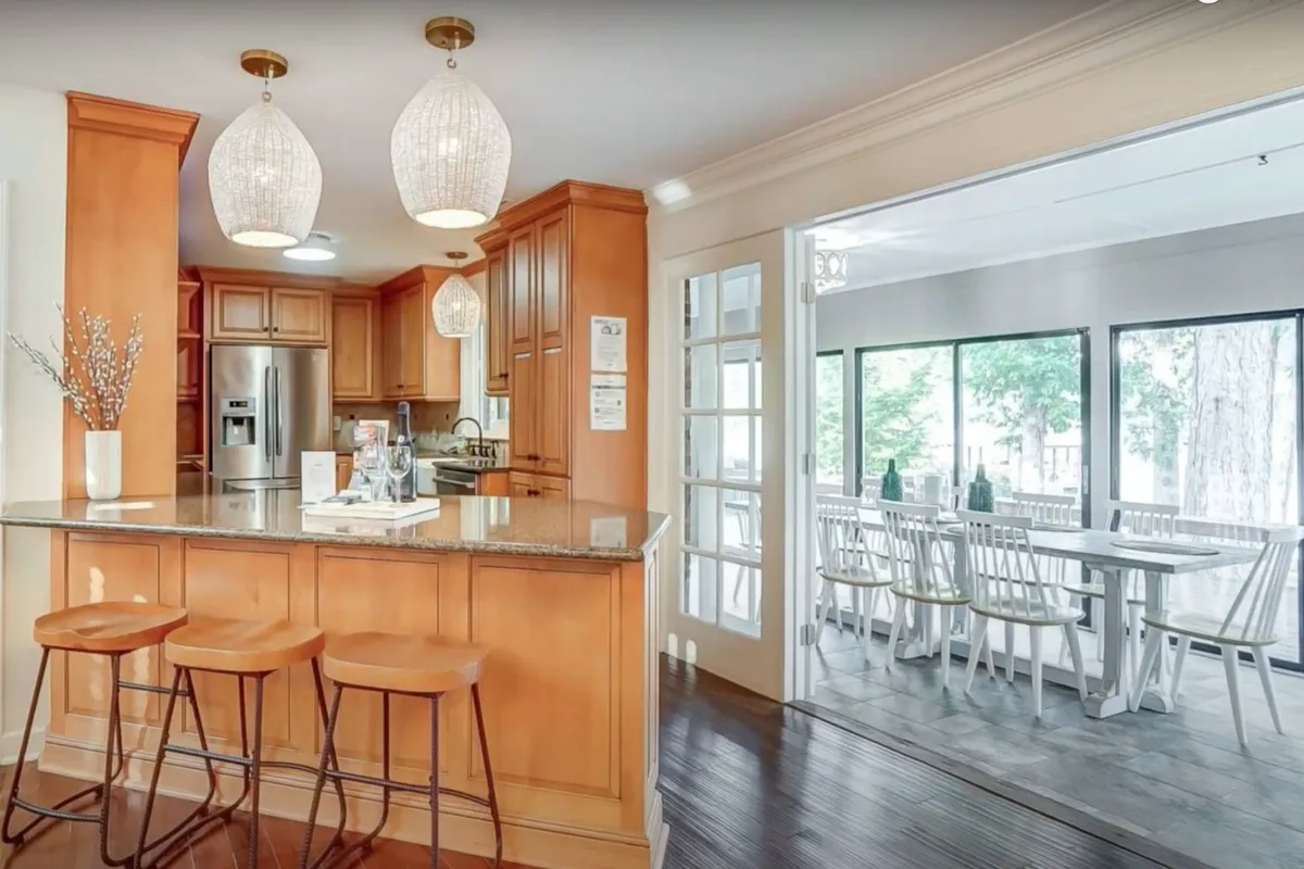 A warm, inviting kitchen scene with a prominent kitchen island beneath stylish pendant lights. Ample counter space, contemporary appliances, and an adjacent dining table create an environment perfect for cooking, gathering, and entertaining. The open layout seamlessly links the kitchen and dining area, encouraging interaction and togetherness.