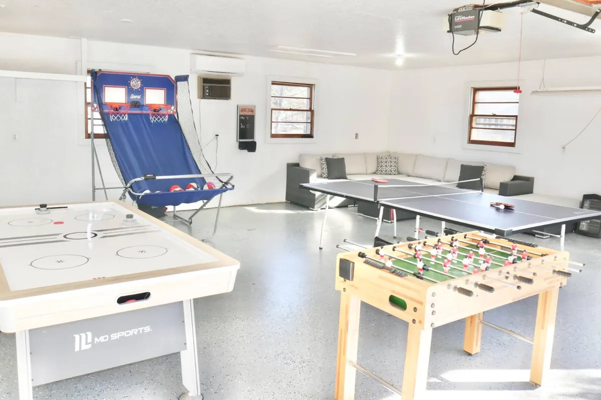 A vibrant game room interior featuring a selection of entertainment options—air hockey, foosball, ping pong, a basketball shooting game, and a comfy couch for lounging between rounds. The playful setup is designed for group fun and family bonding.
