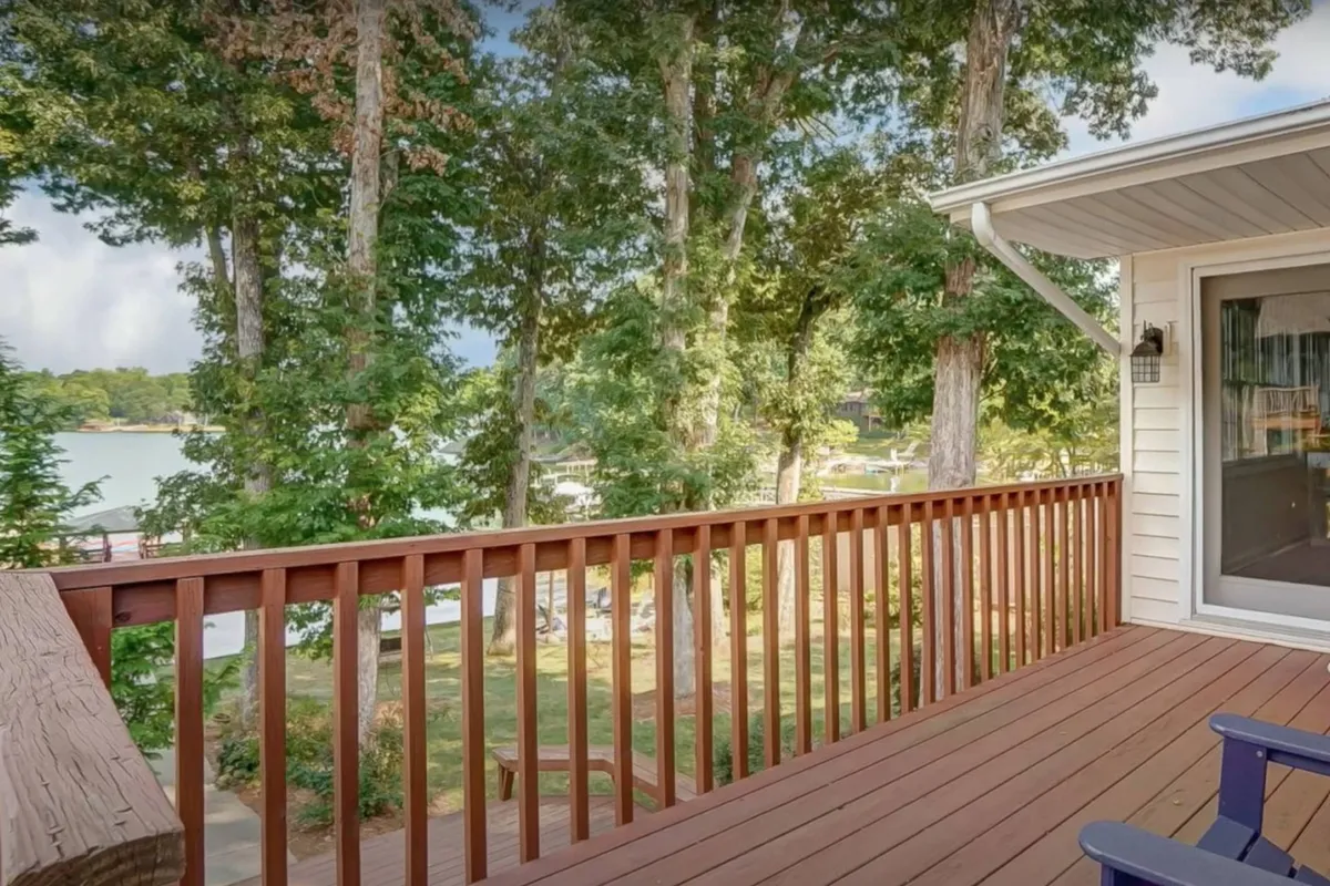 A wide perspective from a deck overlooking the lake, framed by sturdy railings and surrounded by trees. The soft dawning light and clear sky set a tranquil mood, with ample space on the deck for yoga, gatherings, or simply soaking in the scenery.