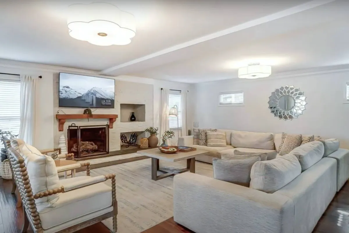 A cozy living room features a large sectional sofa, a welcoming fireplace, and a wall-mounted TV. There's ample plush seating for movie nights or relaxed socializing, and the decor combines comfort with style. The room’s arrangement encourages people to gather and connect.