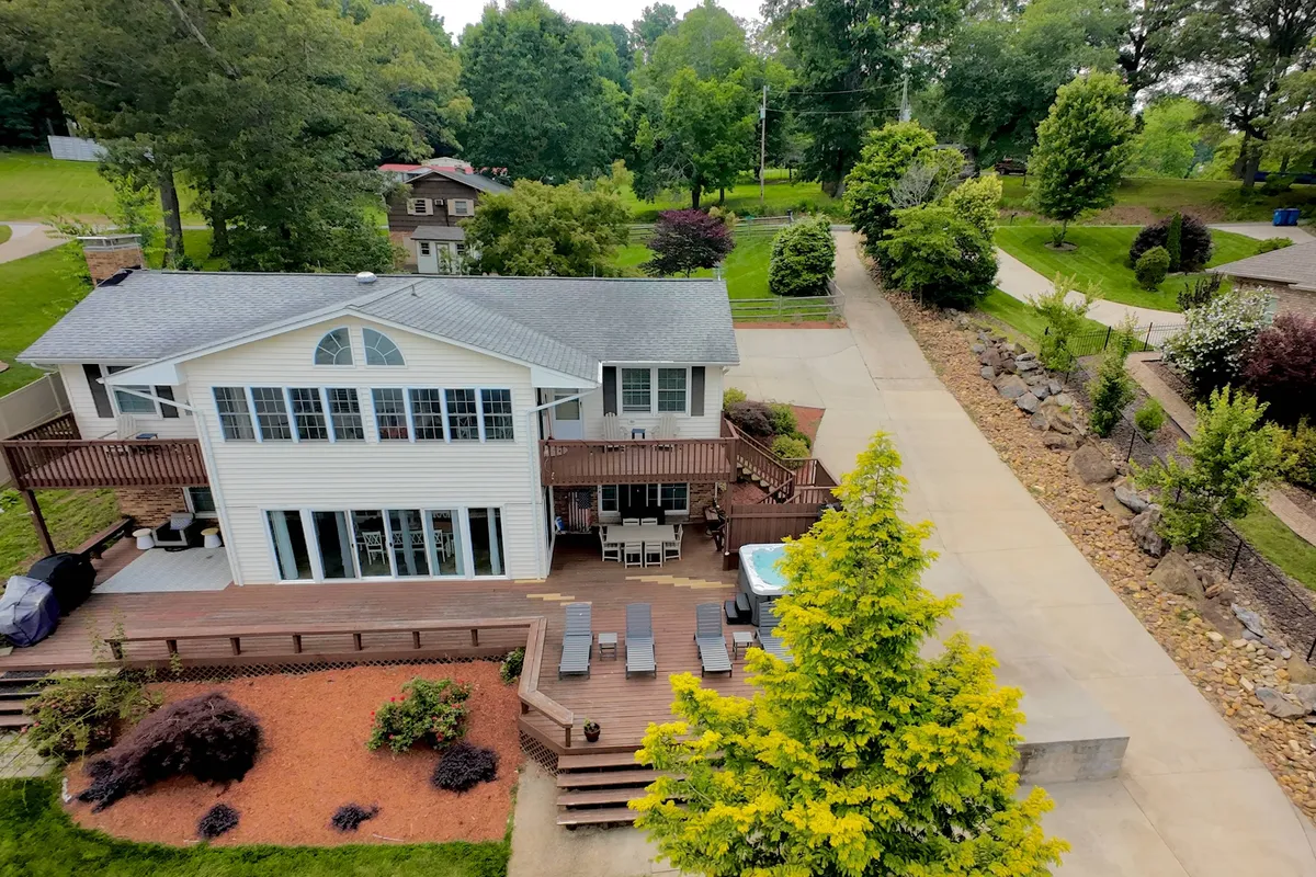 An inviting deck area equipped with a hot tub, surrounded by verdant greenery and the house's welcoming facade in the background. The space is ideal for relaxing soaks, outdoor dining, or enjoying the sunset and nighttime stargazing.