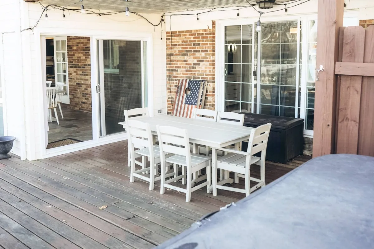 A welcoming outdoor dining table set on a patio, with the house’s sliding glass doors in the background and an American flag waving nearby. The setup is ideal for family gatherings, festive occasions, and relaxing afternoon meals, with hints of the home’s indoor-outdoor flow.