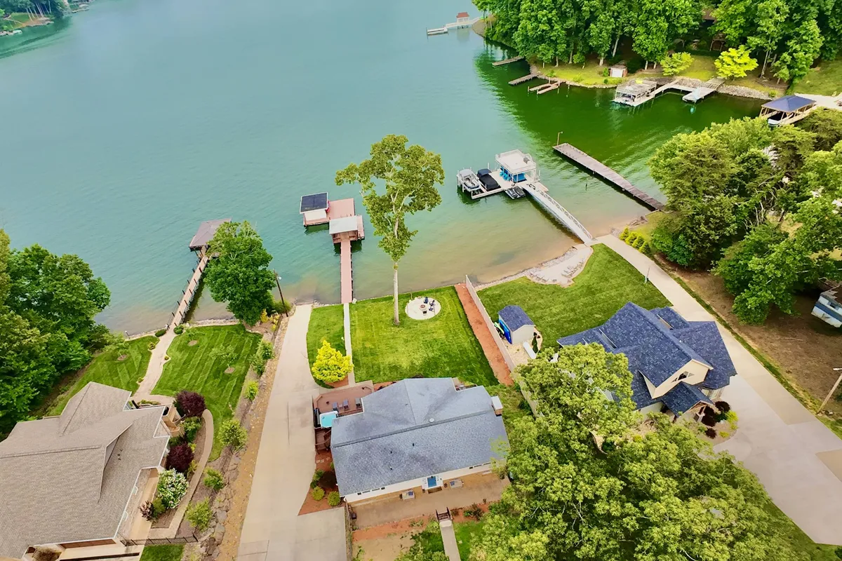 A tranquil lakeside view featuring the calm water, docks, homes dotted along the shoreline, and lush greenery. The setting is peaceful and inviting, with the lake taking center stage as the heart of outdoor relaxation and recreation.