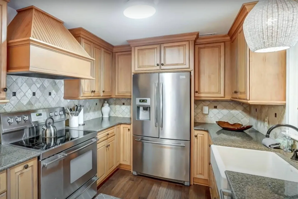 A cozy kitchen with sleek stainless steel appliances, granite countertops, and rich wood cabinetry. A unique light fixture adds a touch of character, while the overall space exudes warmth and functionality, ideal for family gatherings and cooking experiments.